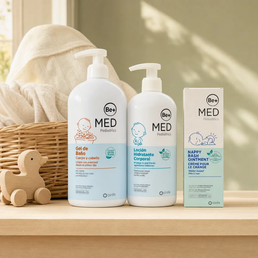 Gel de baño, loción hidratante y crema para el cambio de pañal Be+ Med Pediatrics, junto a una cesta de mimbre con una muselina y un patito de madera